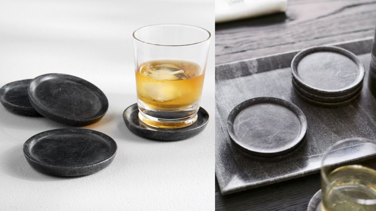 A set of black marble drink coasters displayed on a white and dark wooden surface, with one coaster in use under a whiskey glass filled with ice.