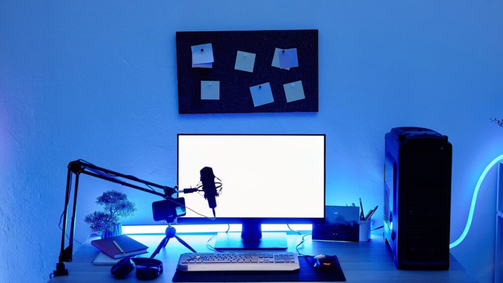 A gaming and streaming setup with a glowing blue theme, featuring a monitor, microphone, keyboard, mouse, and a desktop PC.