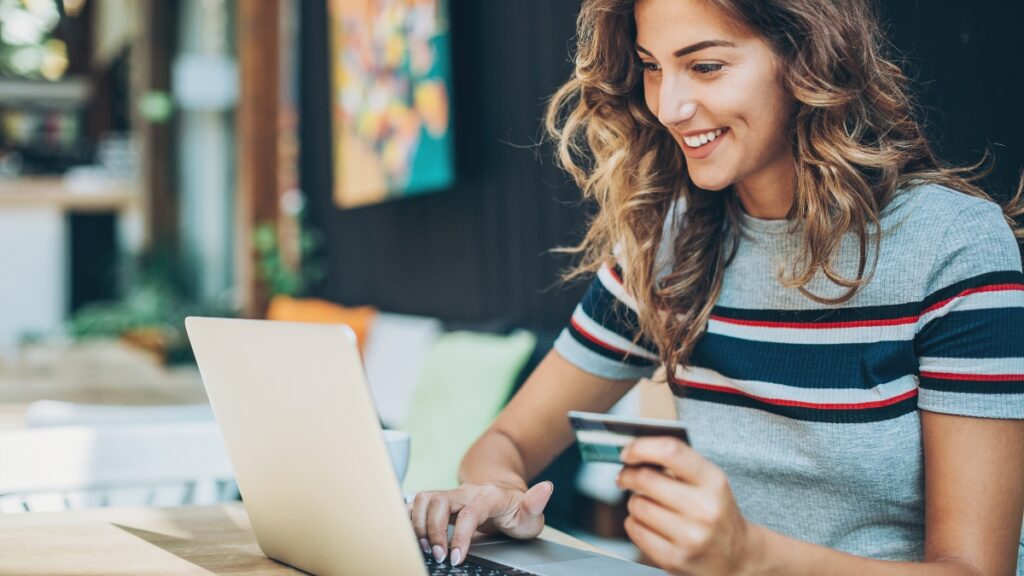 Smiling woman shopping online with a laptop and credit card at a cozy cafe.