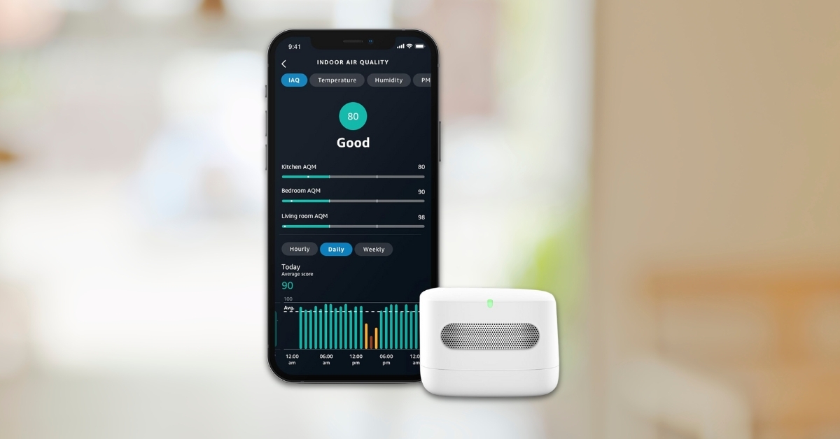 Amazon Smart Air Quality Monitor displayed next to smartphone app showing indoor air quality score, temperature, humidity, and PM levels in a modern home setting